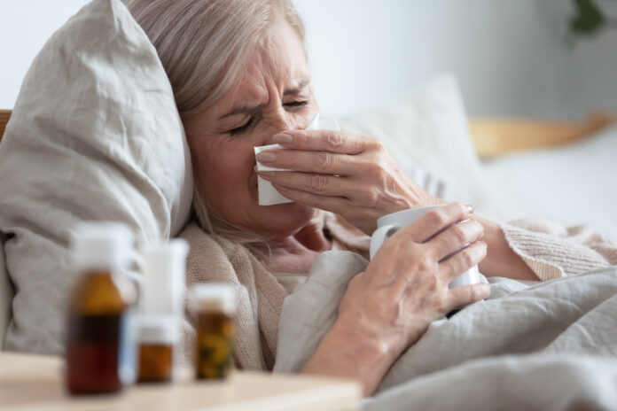 Przeziębienie - leżąca w łóżku starsza kobieta z katarem