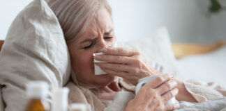 Przeziębienie - leżąca w łóżku starsza kobieta z katarem